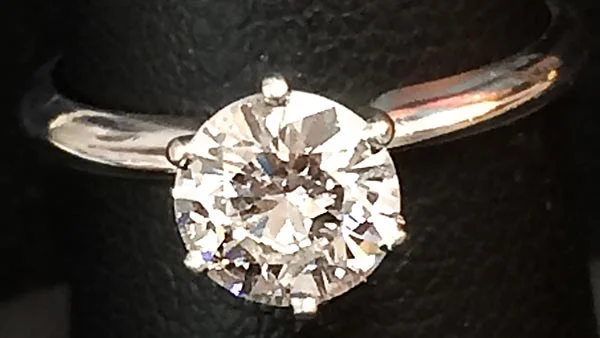 Classic solitaire diamond engagement ring set in white gold on a black background.