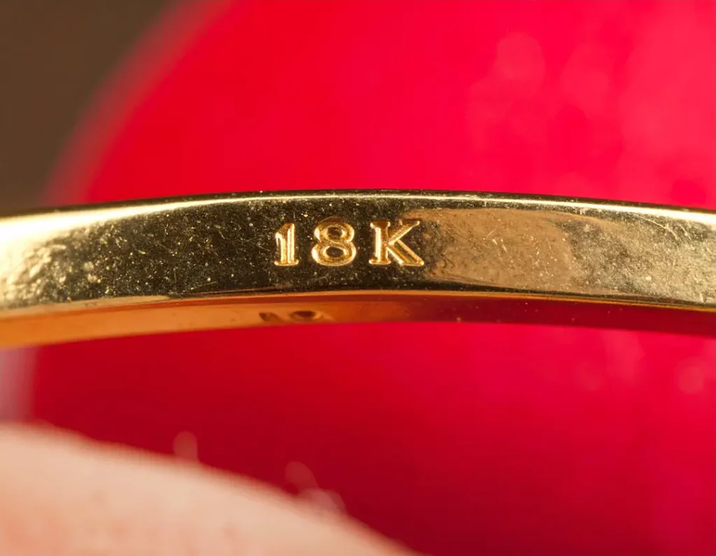 Macro view of an 18K engraving inside a gold ring band showing authenticity hallmark detail.