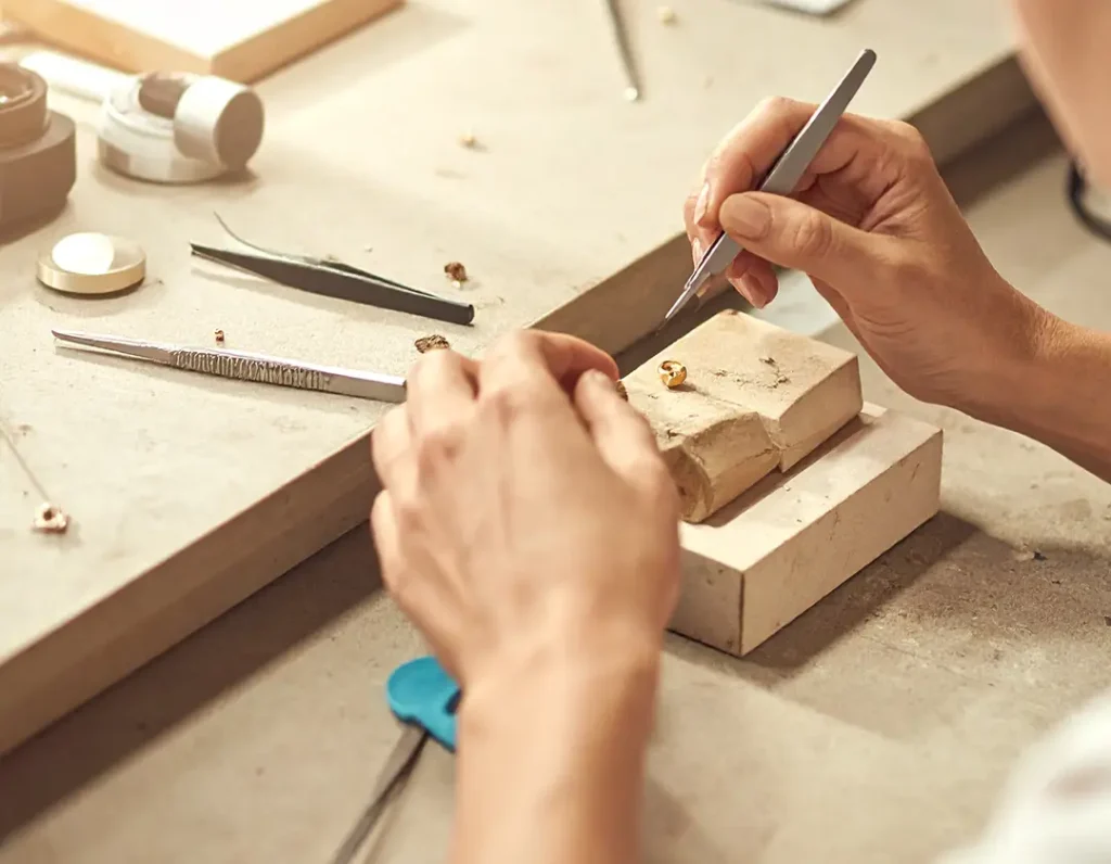 Jeweler testing a piece of gold jewelry on a workbench using precision tools in warm daylight.