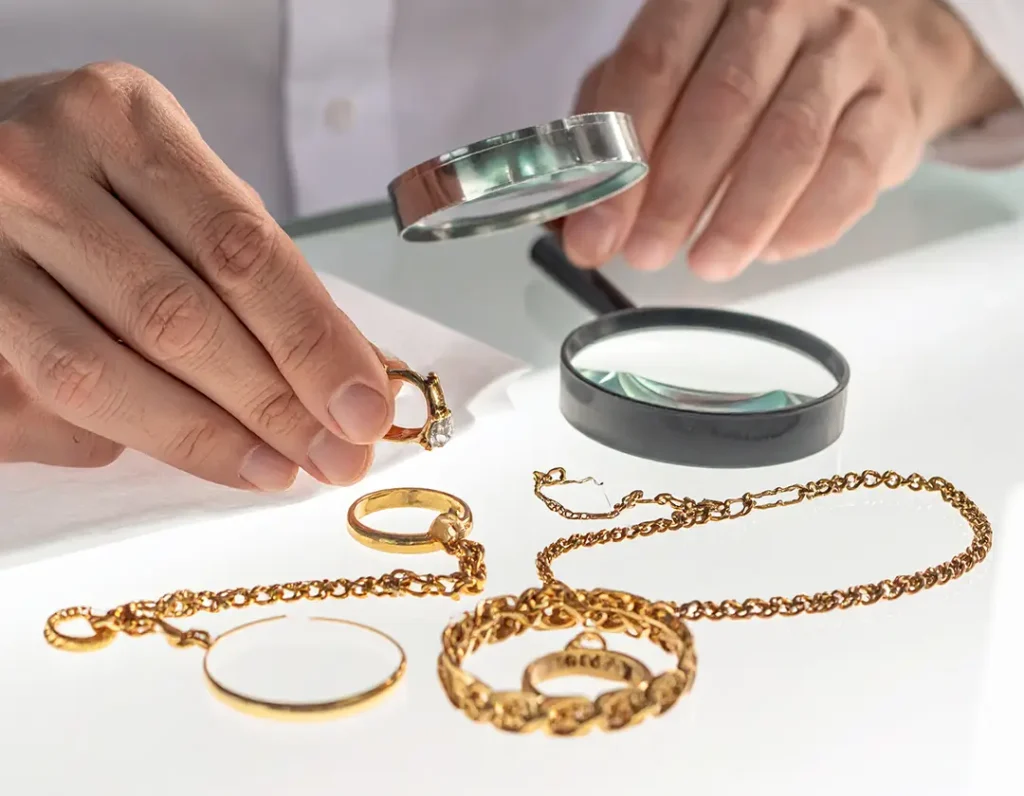 Jeweler’s hands examining gold rings and chains under warm light on a glass jewelry counter.