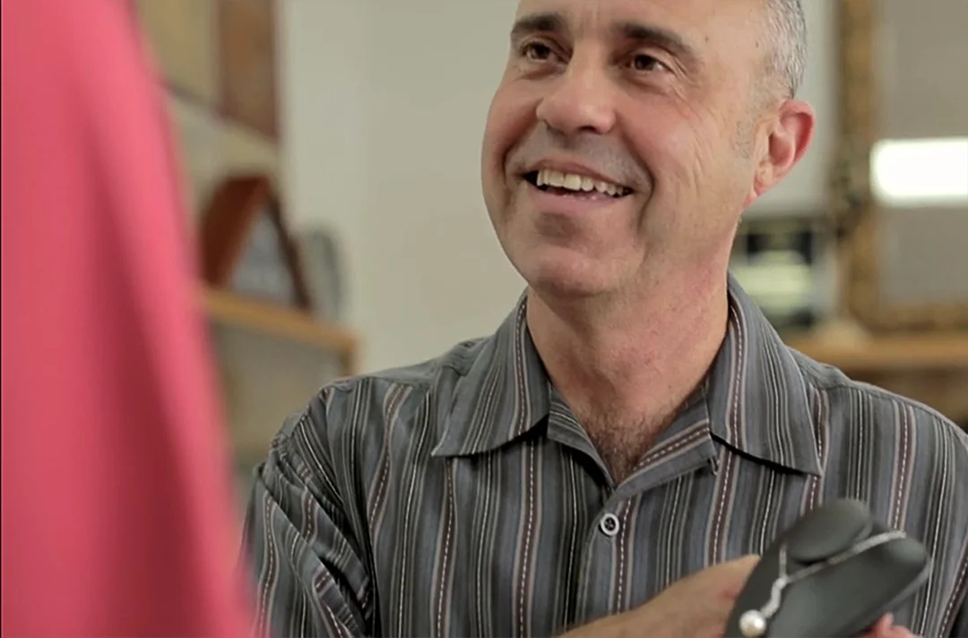 Paul Potenza, goldsmith and co-owner of Design One Jewelers, smiling while showing a necklace to a customer in the store.